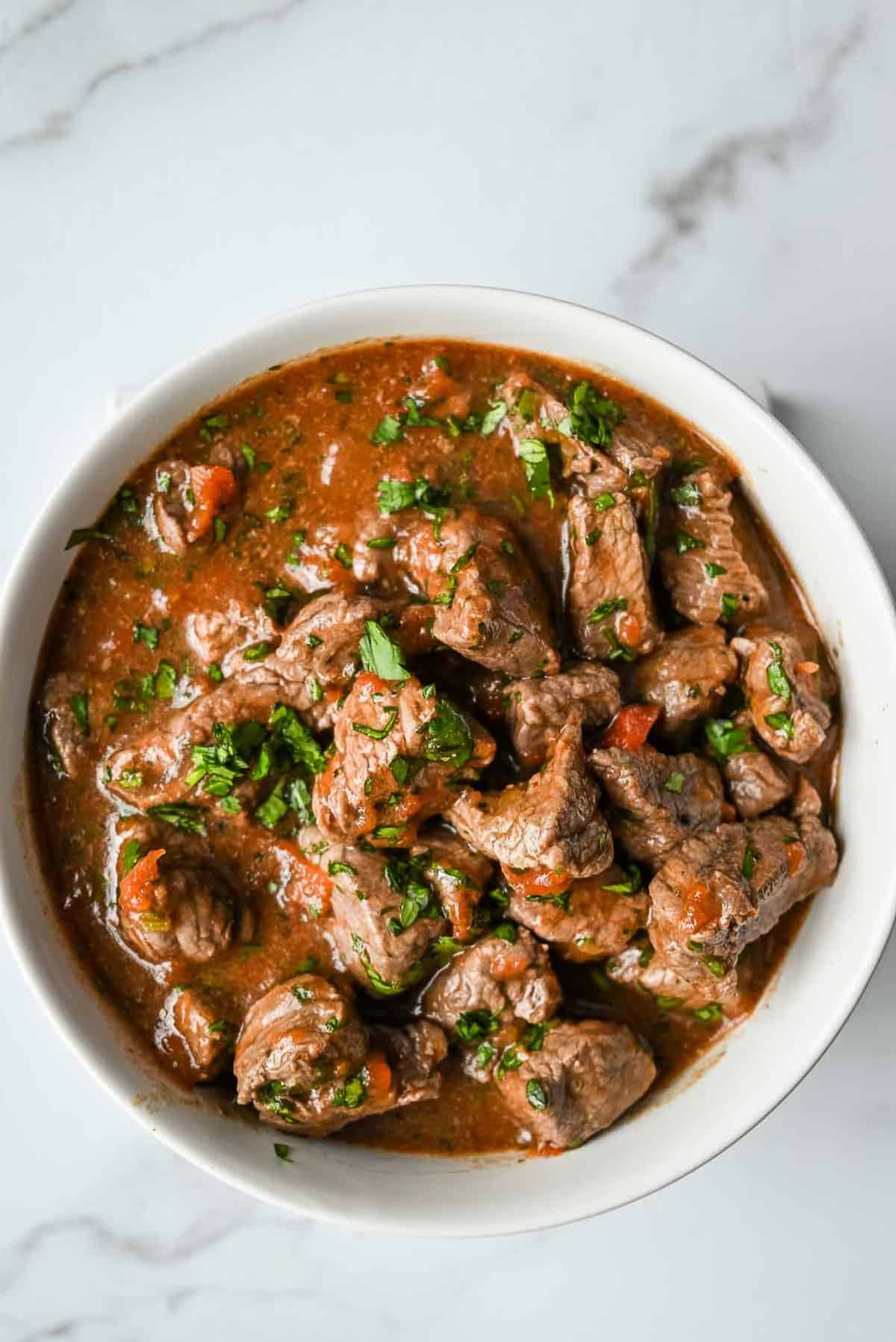 bowl of carne asada topped with cilantro on a white background