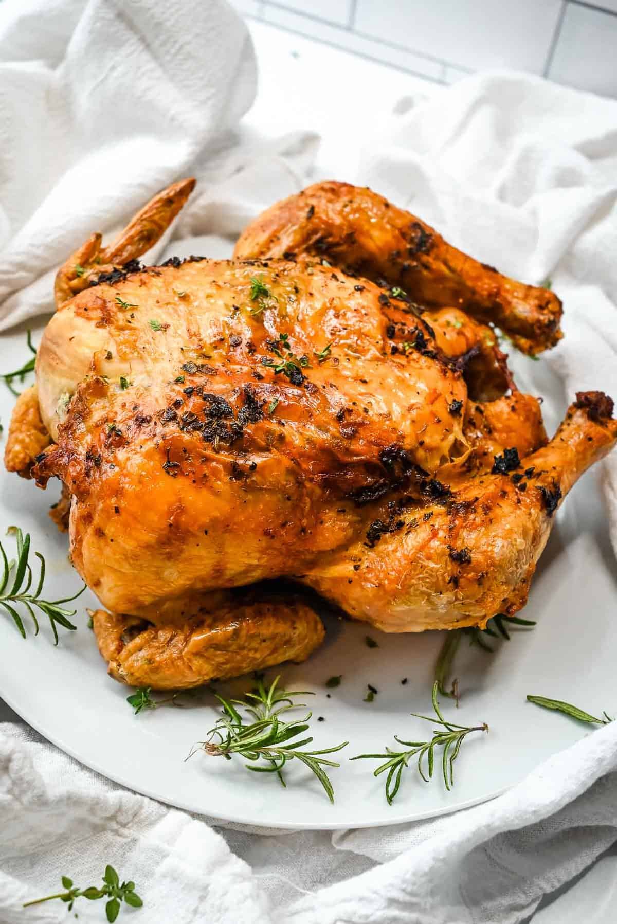 ninja foodi whole chicken cooked on a white plate topped with herbs.