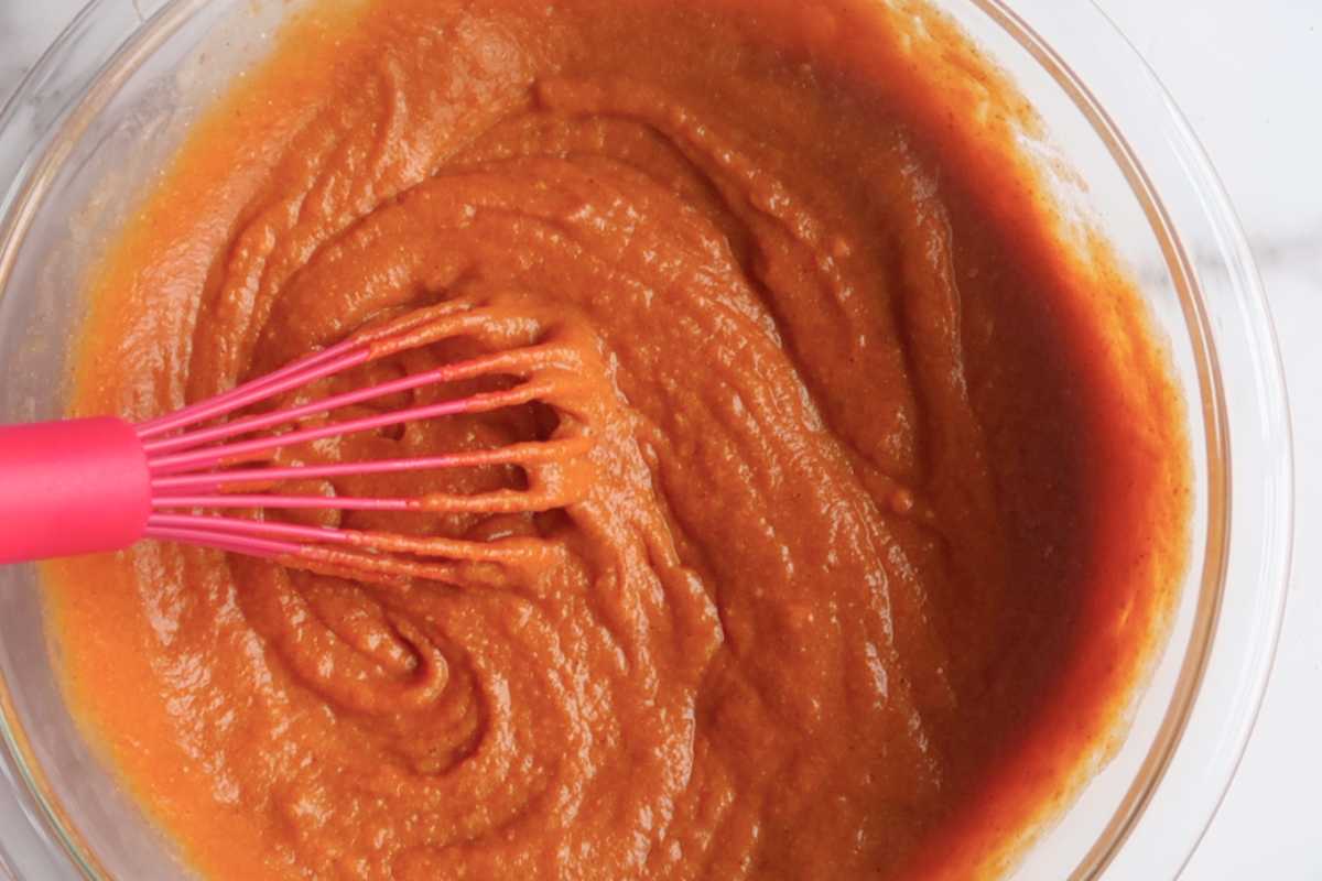 pumpkin pie filling in a glass bowl with a pink whisk.